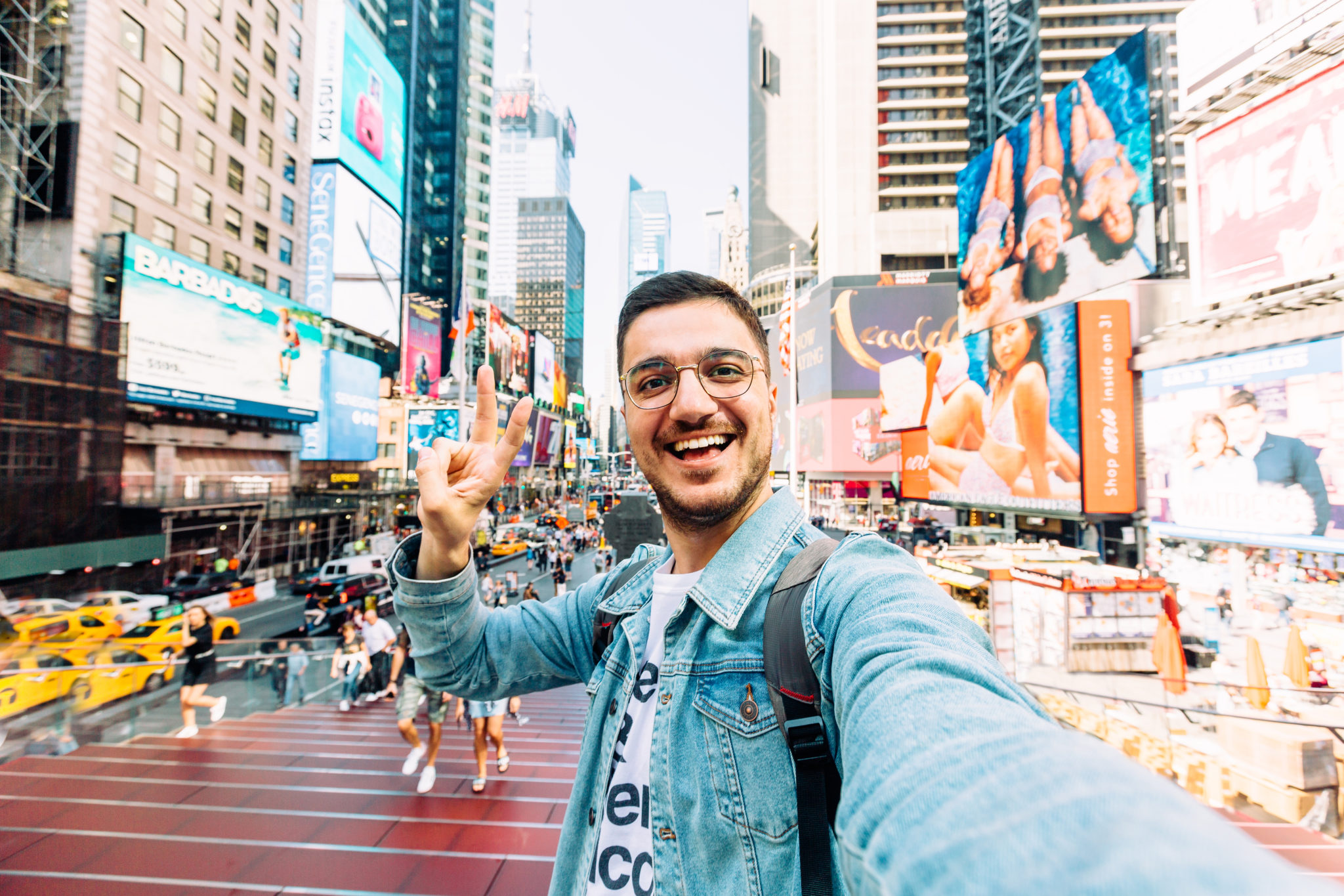 Young happy man taking selfie and showing peace gesture at Times Square