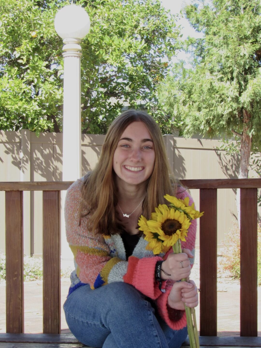 APU student Emily Chew sits on a bench smiling and holding a bouquet of sunflowers.